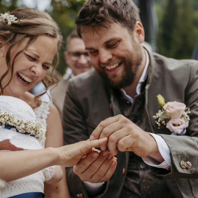 Julia und Andreas bei ihrer Hochzeit auf der Hatzalm in Hintersee in traditioneller Tracht mit Bergkulisse im Hintergrund.