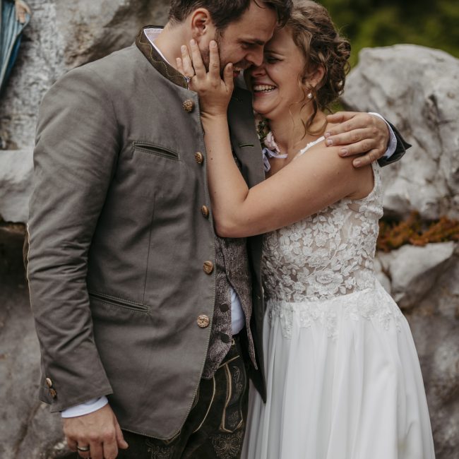 Julia und Andreas bei ihrer Hochzeit auf der Hatzalm in Hintersee in traditioneller Tracht mit Bergkulisse im Hintergrund.