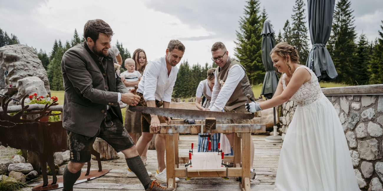 Julia und Andreas bei ihrer Hochzeit auf der Hatzalm in Hintersee in traditioneller Tracht mit Bergkulisse im Hintergrund.