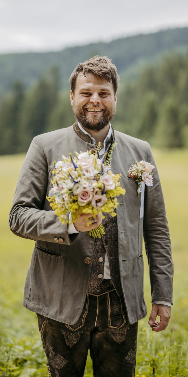 Julia und Andreas bei ihrer Hochzeit auf der Hatzalm in Hintersee in traditioneller Tracht mit Bergkulisse im Hintergrund.