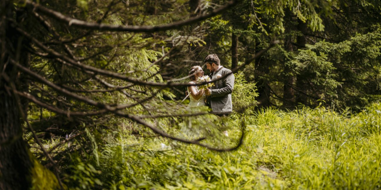 Julia und Andreas bei ihrer Hochzeit auf der Hatzalm in Hintersee in traditioneller Tracht mit Bergkulisse im Hintergrund.