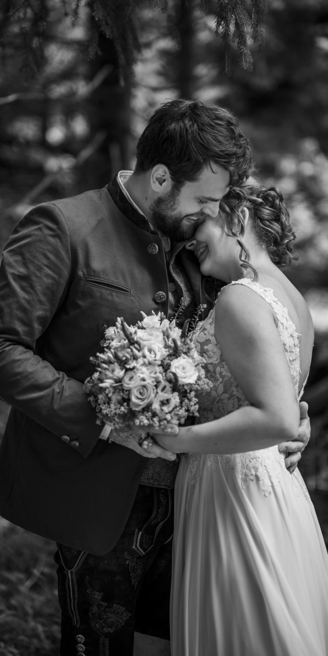 Julia und Andreas bei ihrer Hochzeit auf der Hatzalm in Hintersee in traditioneller Tracht mit Bergkulisse im Hintergrund.