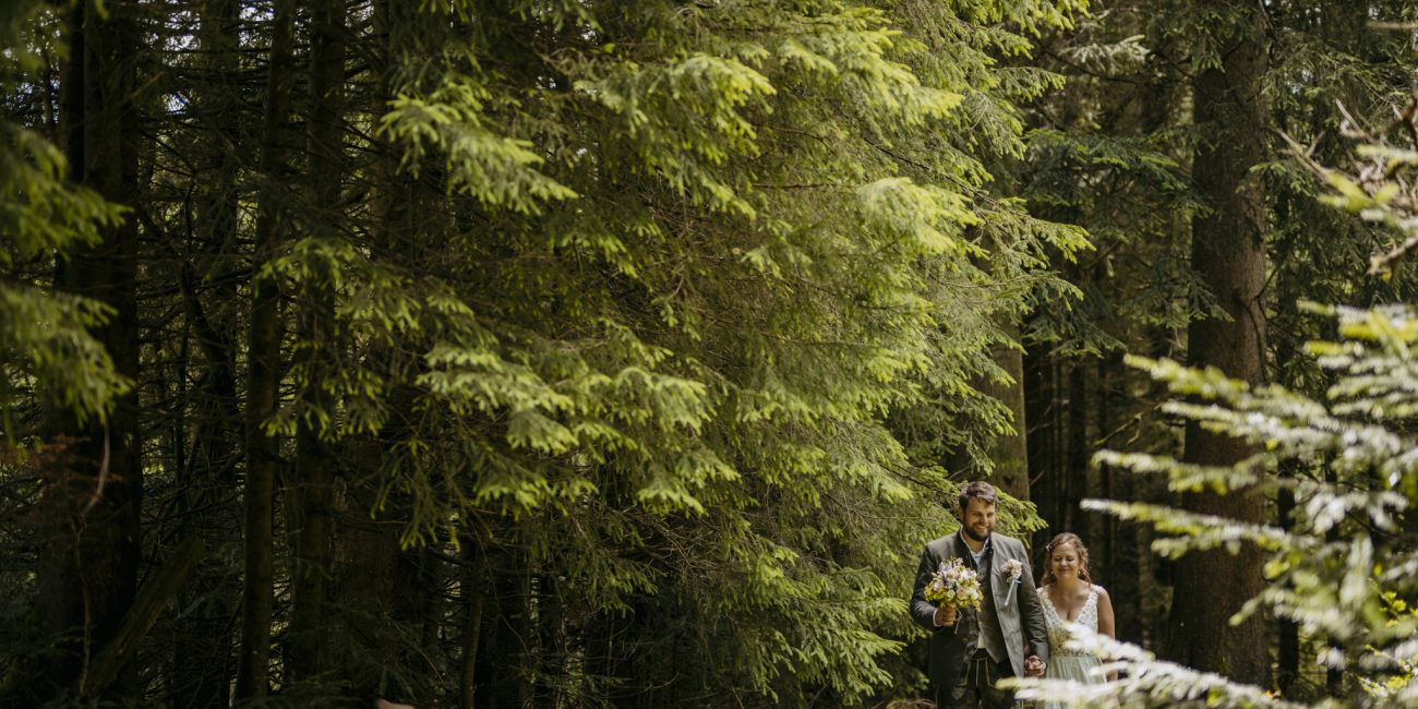 Julia und Andreas bei ihrer Hochzeit auf der Hatzalm in Hintersee in traditioneller Tracht mit Bergkulisse im Hintergrund.