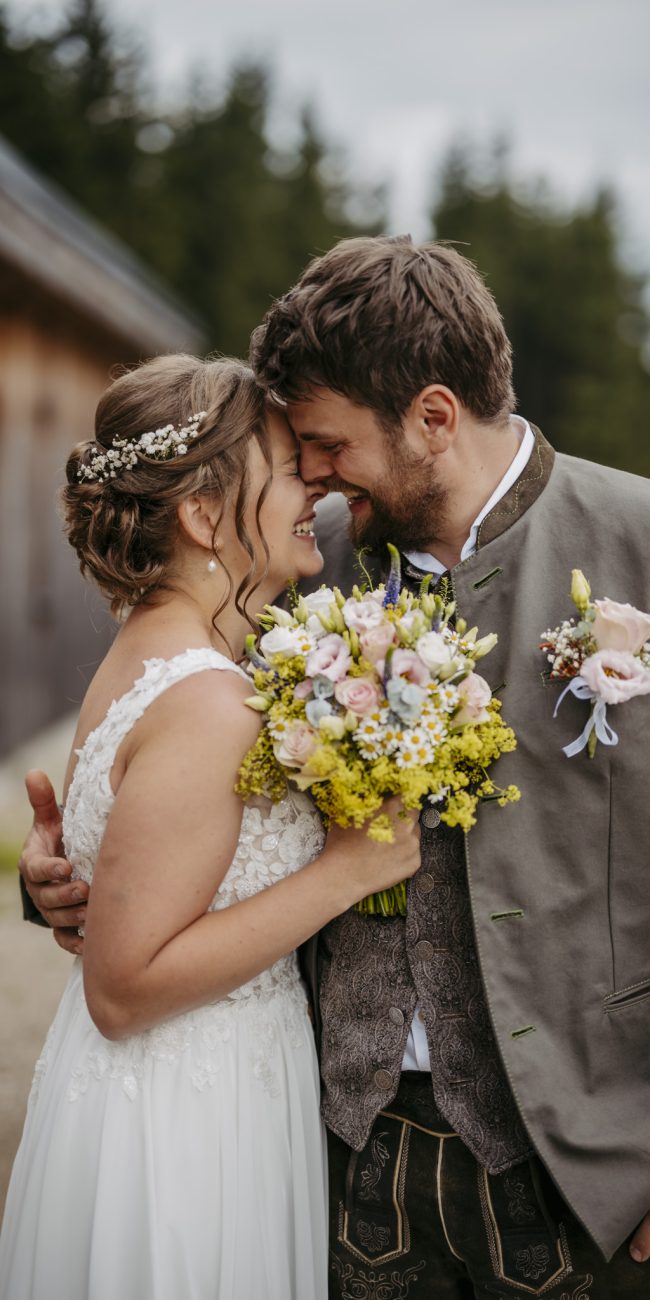 Julia und Andreas bei ihrer Hochzeit auf der Hatzalm in Hintersee in traditioneller Tracht mit Bergkulisse im Hintergrund.