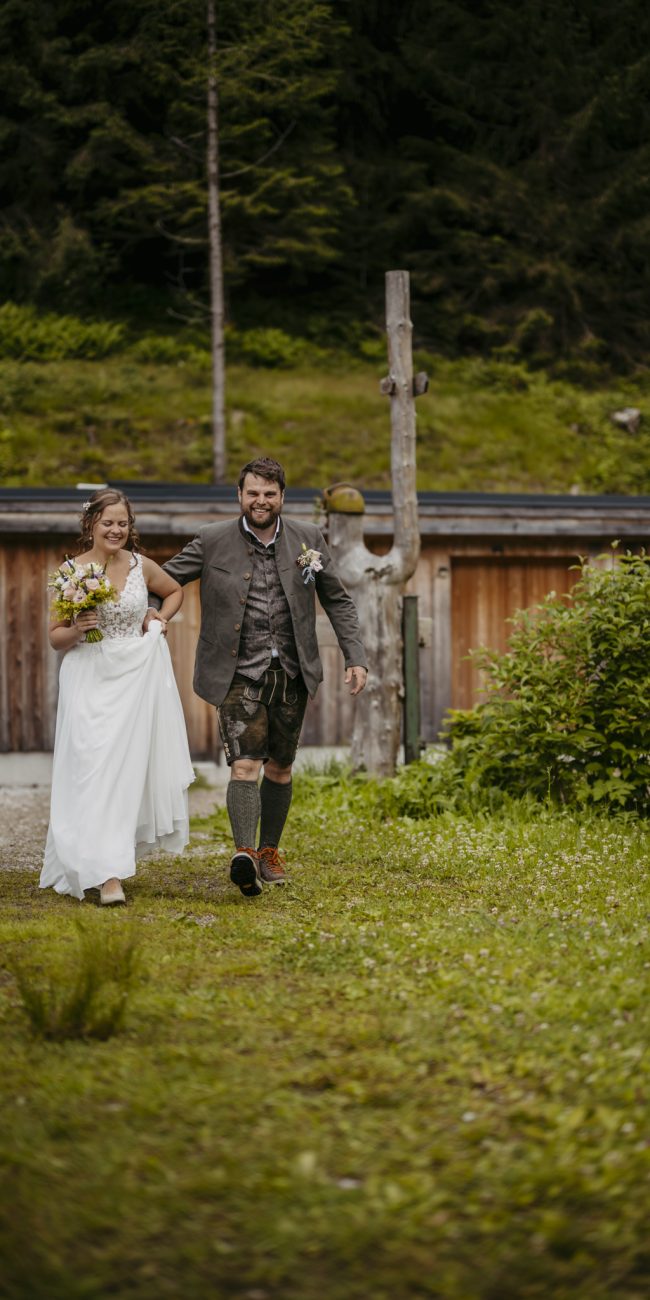 Julia und Andreas bei ihrer Hochzeit auf der Hatzalm in Hintersee in traditioneller Tracht mit Bergkulisse im Hintergrund.