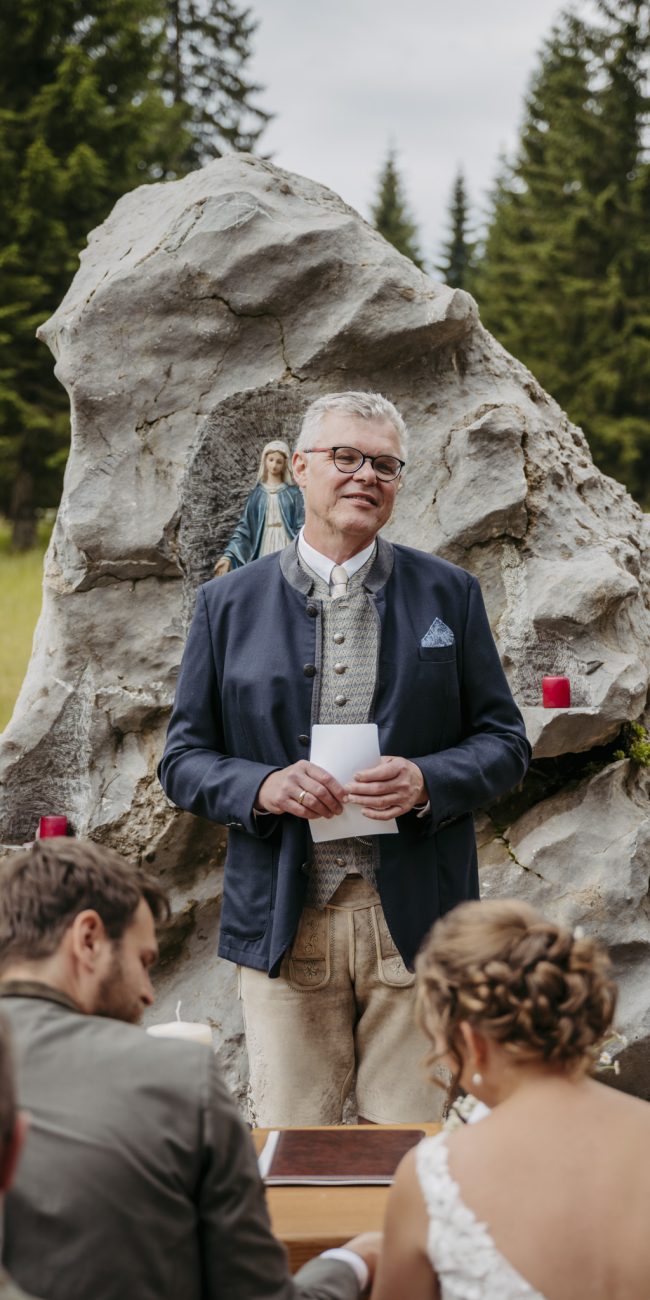 Julia und Andreas bei ihrer Hochzeit auf der Hatzalm in Hintersee in traditioneller Tracht mit Bergkulisse im Hintergrund.